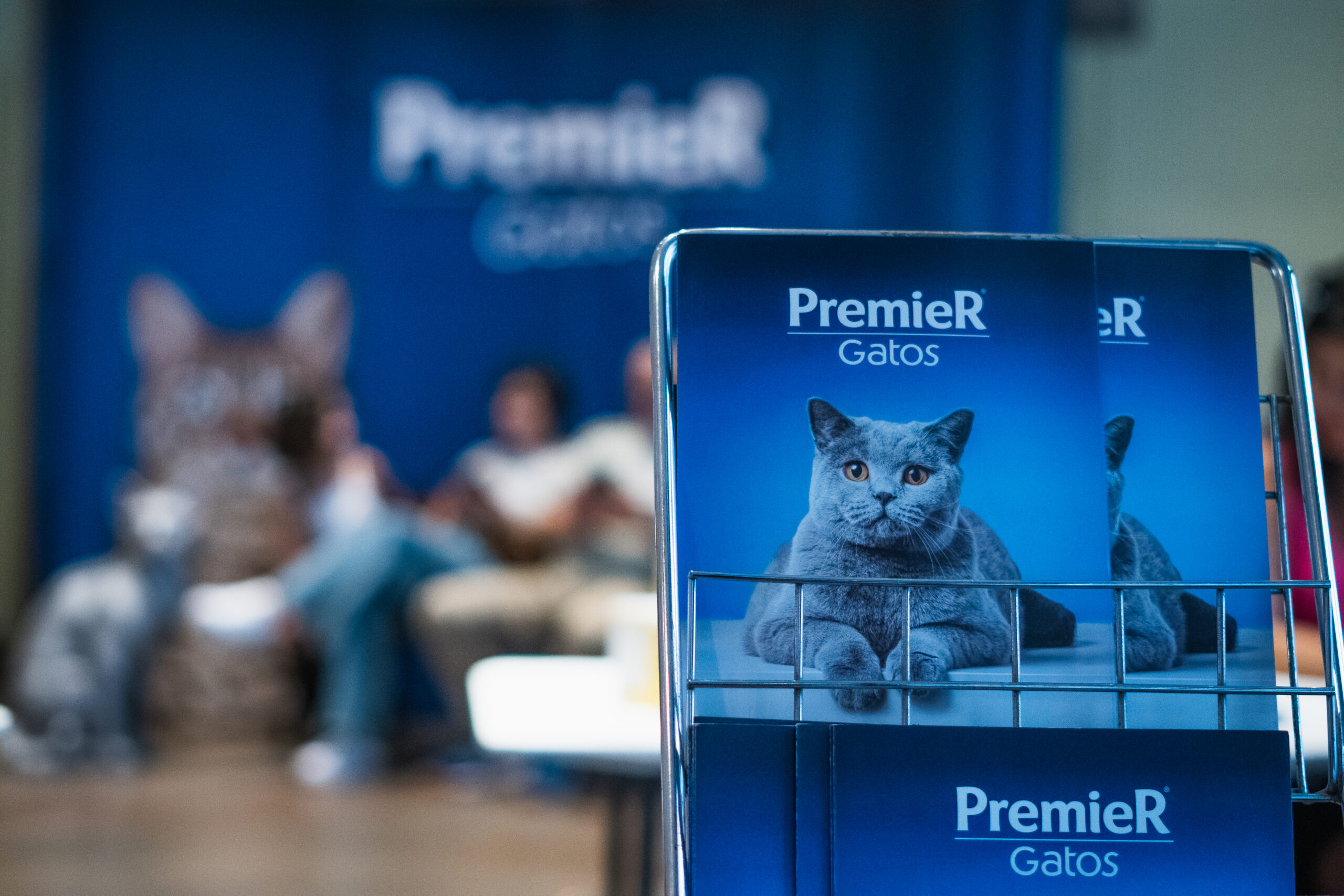 Revista da PremieR® Gatos em primeiro plano, com um banner de fundo sobre o evento da PremieR® Gatos