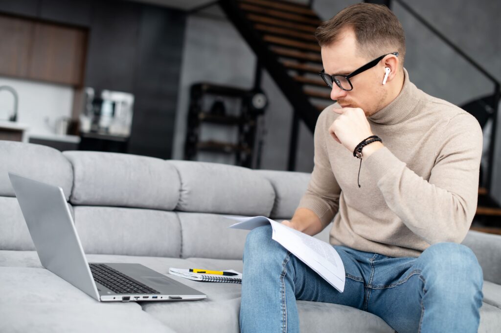 Homem olhando para o computador com seu caderno apoiado na perna direita