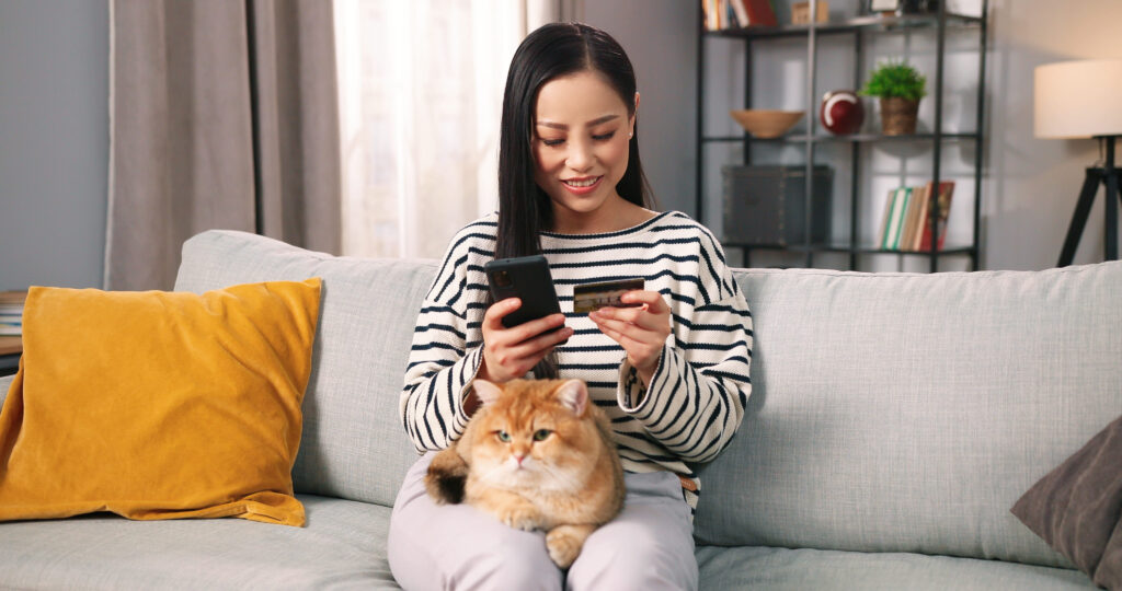 Mulher com seu celular e cartão nas mãos, enquanto seu gato está sobre sua perna