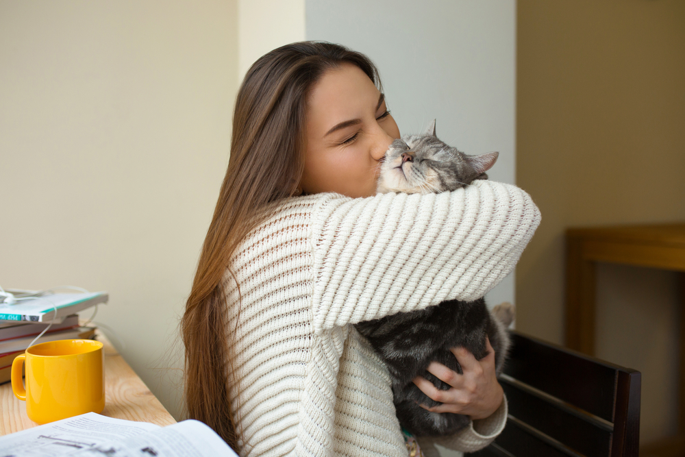 Mulher beijando e abraçando gato cinza