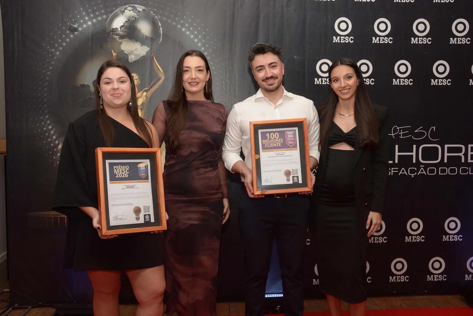 4 pessoas recebendo 2 prêmios em cerimônia